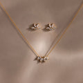 The Marquise Diamond Jewelry Set features a gold necklace and earrings with leaf-shaped diamond designs, ideal for weddings. This set sparkles beautifully against a soft brown background.