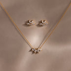 The Marquise Diamond Jewelry Set features a gold necklace and earrings with leaf-shaped diamond designs, ideal for weddings. This set sparkles beautifully against a soft brown background.