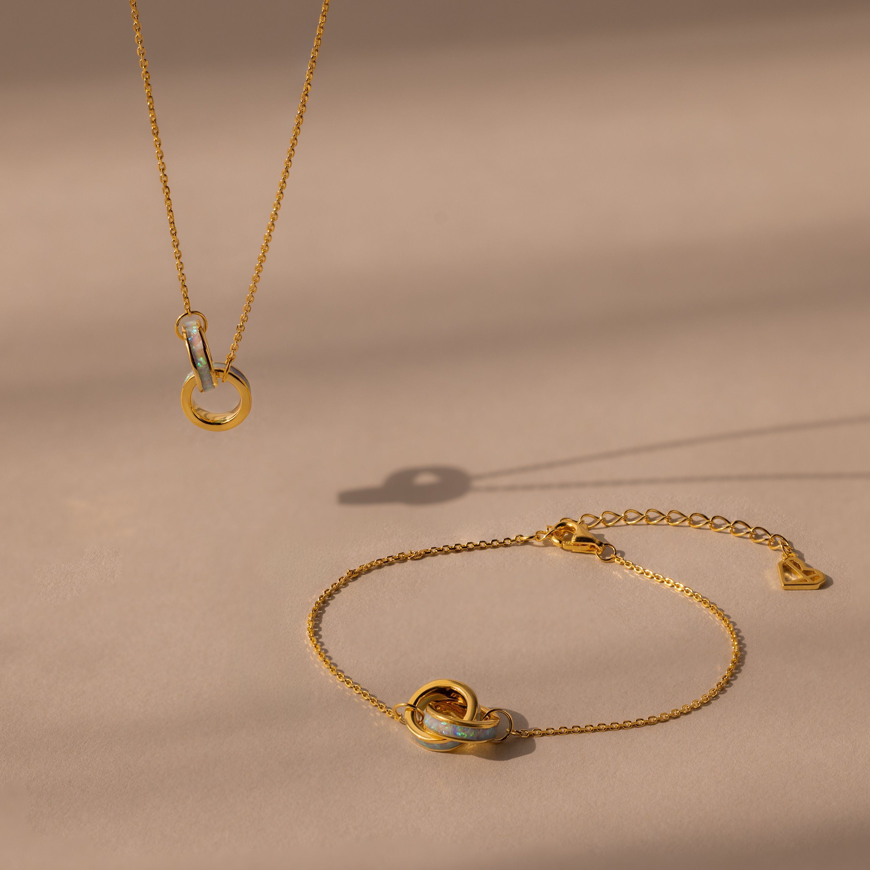 Interlocking Opal Inlay Necklace and Bracelet Set, elegantly displayed on a beige surface with soft shadows.