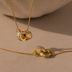 Interlocking Opal Inlay Necklace and Bracelet Set in 18K Gold, featuring white and opal-like enamel accents on interlocking rings, displayed on a beige background.