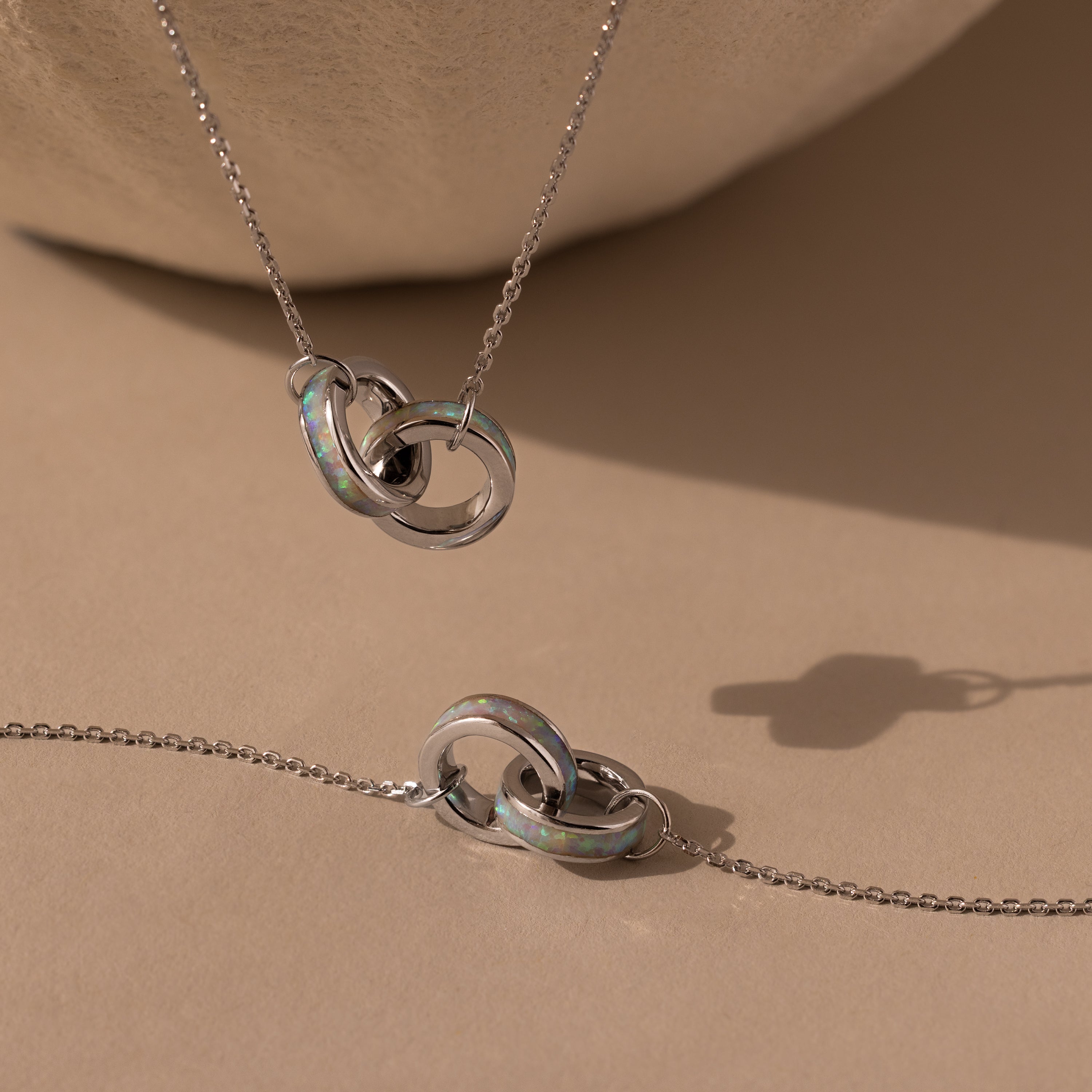 Interlocking Opal Inlay Necklace and Bracelet Set in Silver, featuring iridescent details and opal inlay, elegantly displayed on a beige surface.