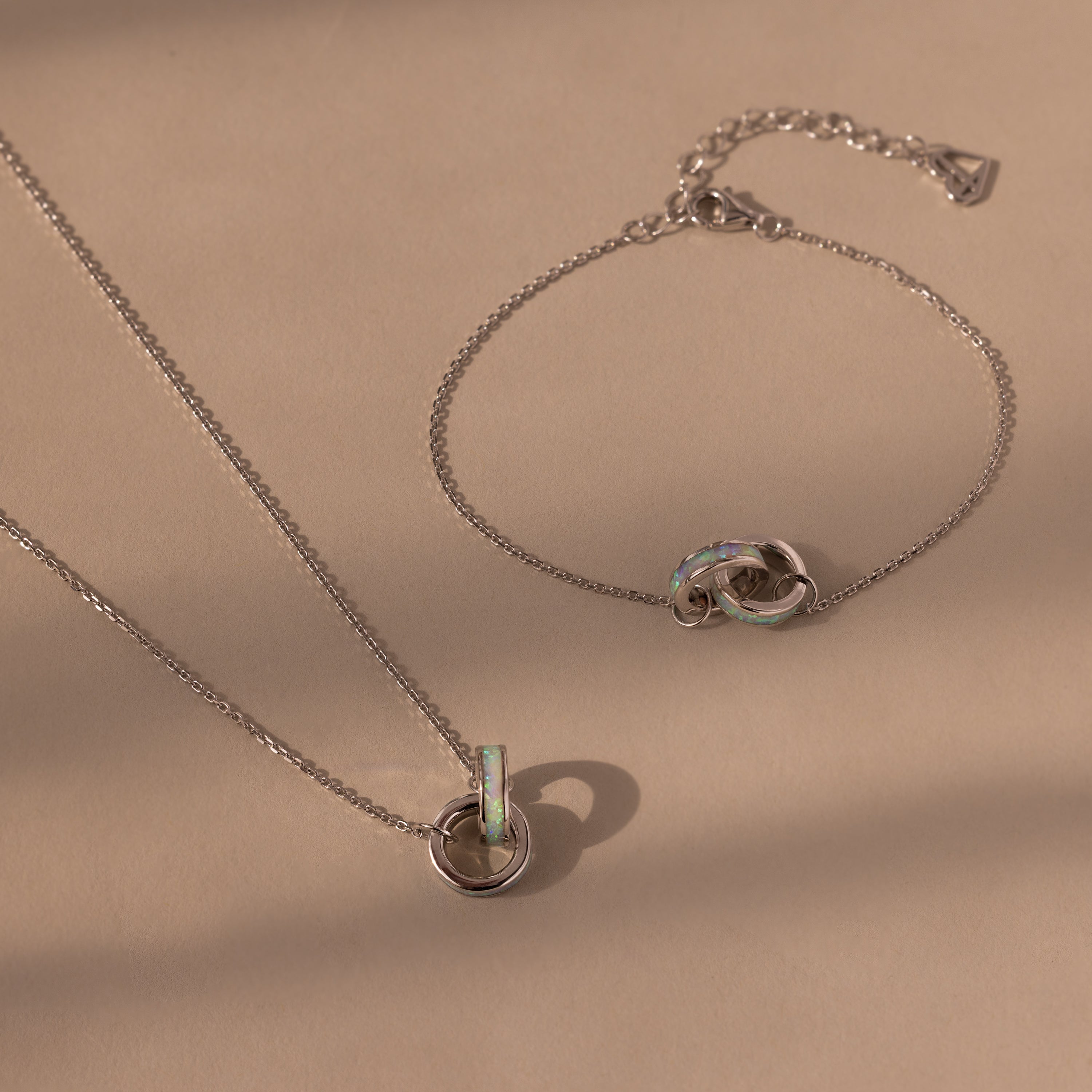 The Interlocking Opal Inlay Necklace and Bracelet Set in Silver features elegant interlocking circle pendants, displayed on a beige background—ideal for lovers of timeless Interlocking Rings Jewelry.
