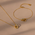 The Interlocking Opal Inlay Necklace and Bracelet Set in 18K Gold features delicate chains and interlocking rings, displayed on a beige background.