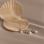 The Pearl Knot Necklace & Earrings Set in Sterling Silver is displayed on a beige shell-shaped dish against a neutral background.