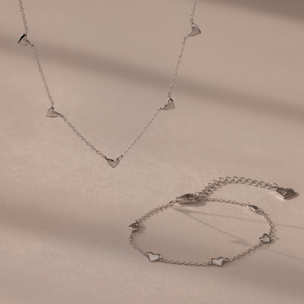 Heart Station Necklace & Bracelet Set in Sterling Silver with small heart charms displayed on a beige surface.