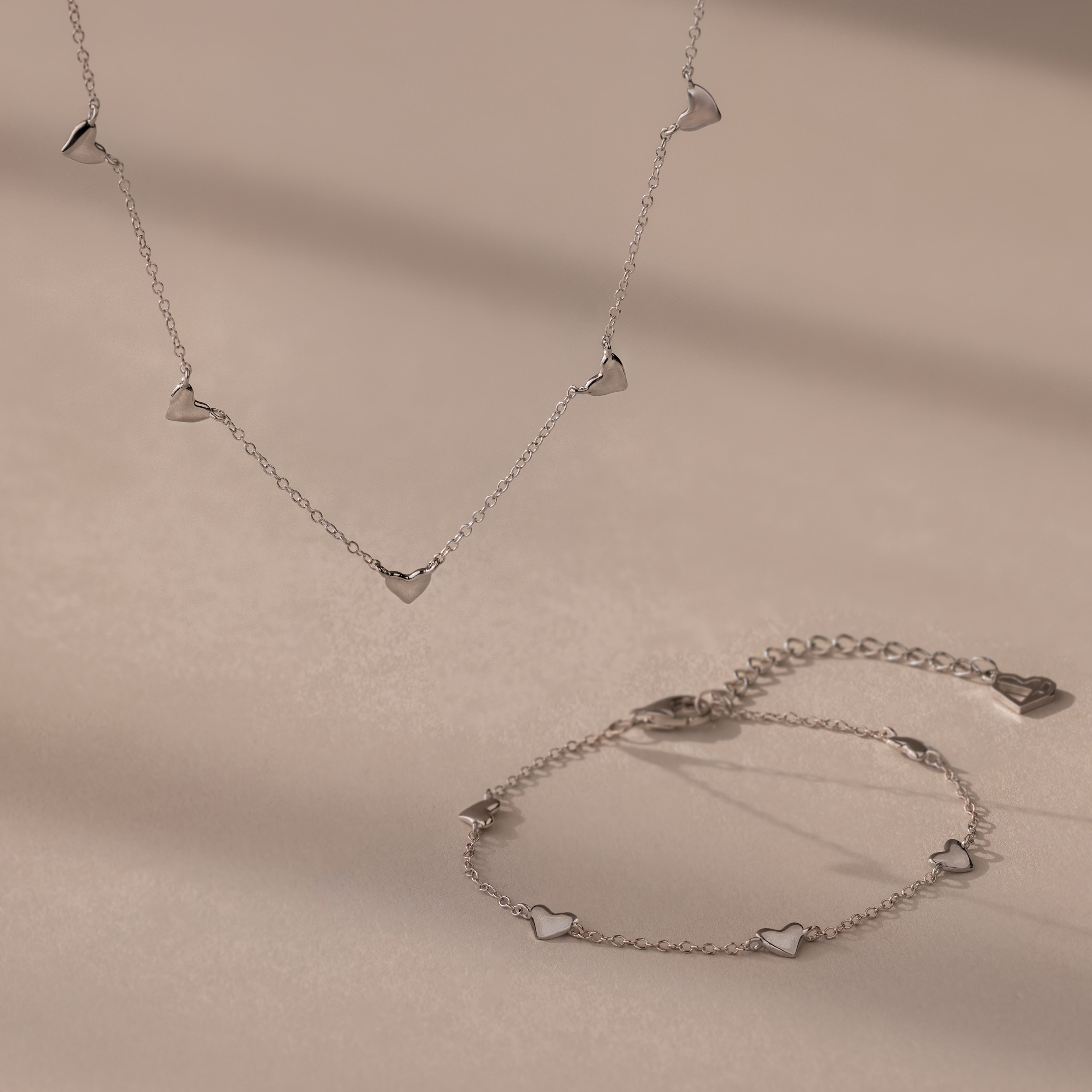 Heart Station Necklace & Bracelet Set in Sterling Silver with small heart charms displayed on a beige surface.