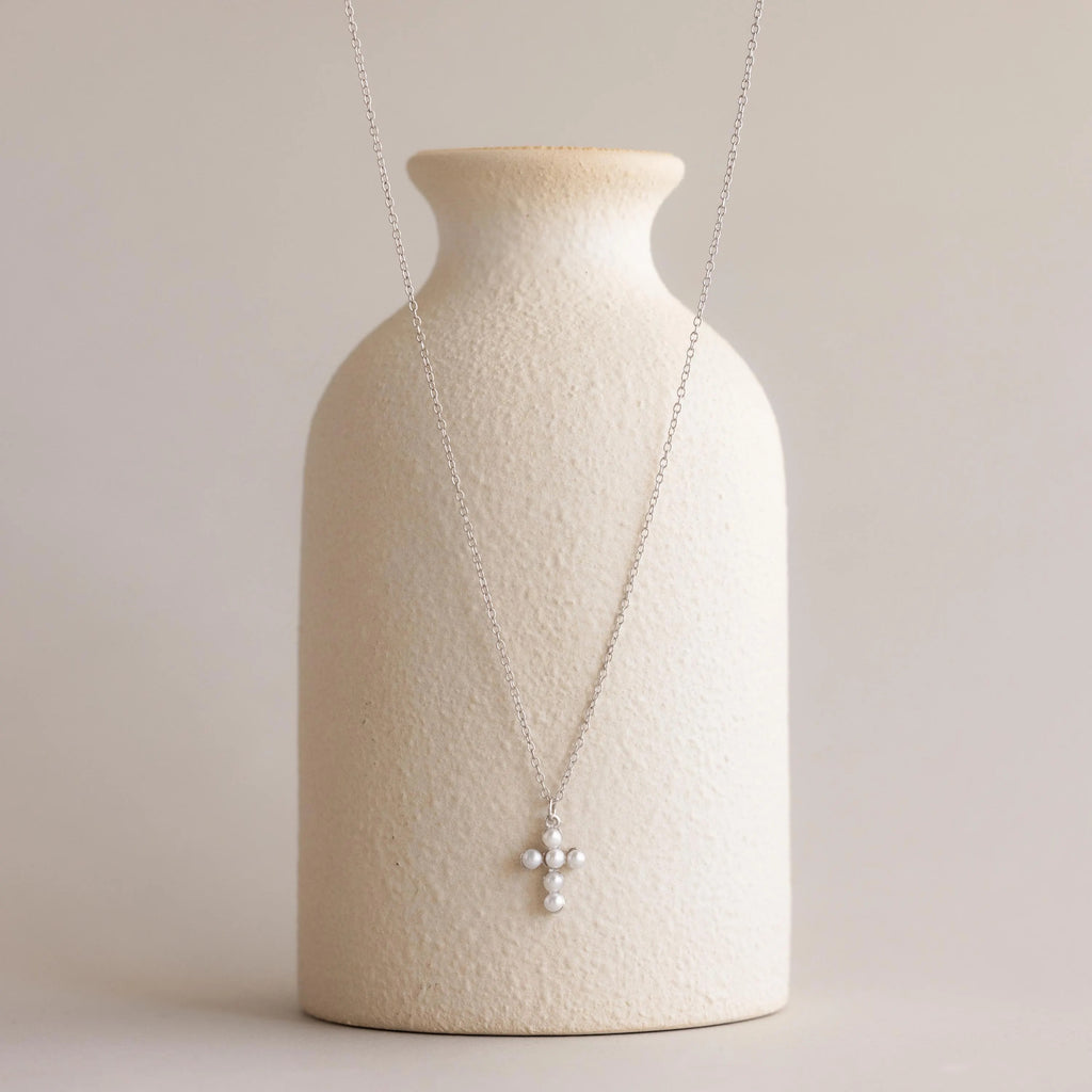 Pearl Cross Necklace adorned with luminous pearls, elegantly displayed on a textured cream vase.