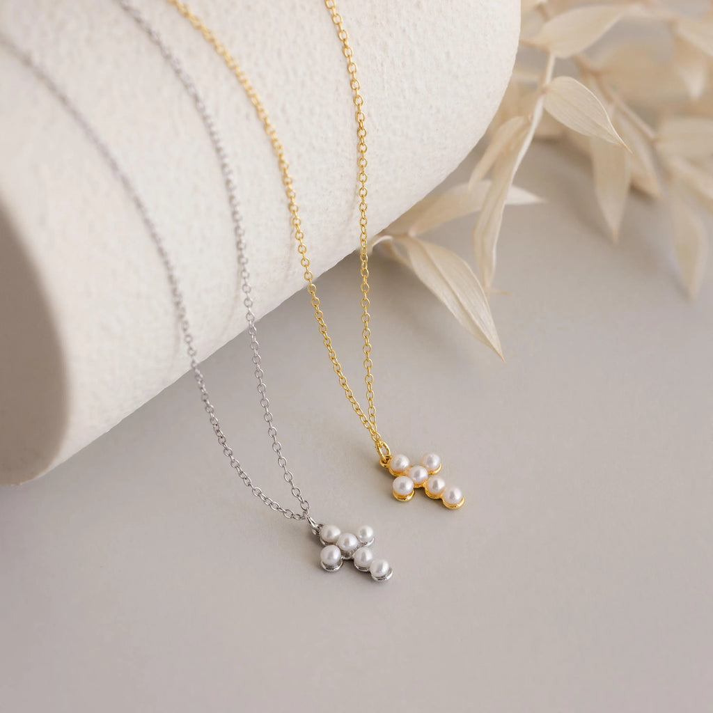 Two Pearl Cross Necklaces, one silver and one gold, with luminous pearl cluster pendants, displayed on a neutral surface.