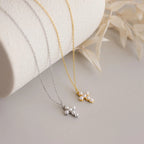 Two Pearl Cross Necklaces, one silver and one gold, with luminous pearl cluster pendants, displayed on a neutral surface.