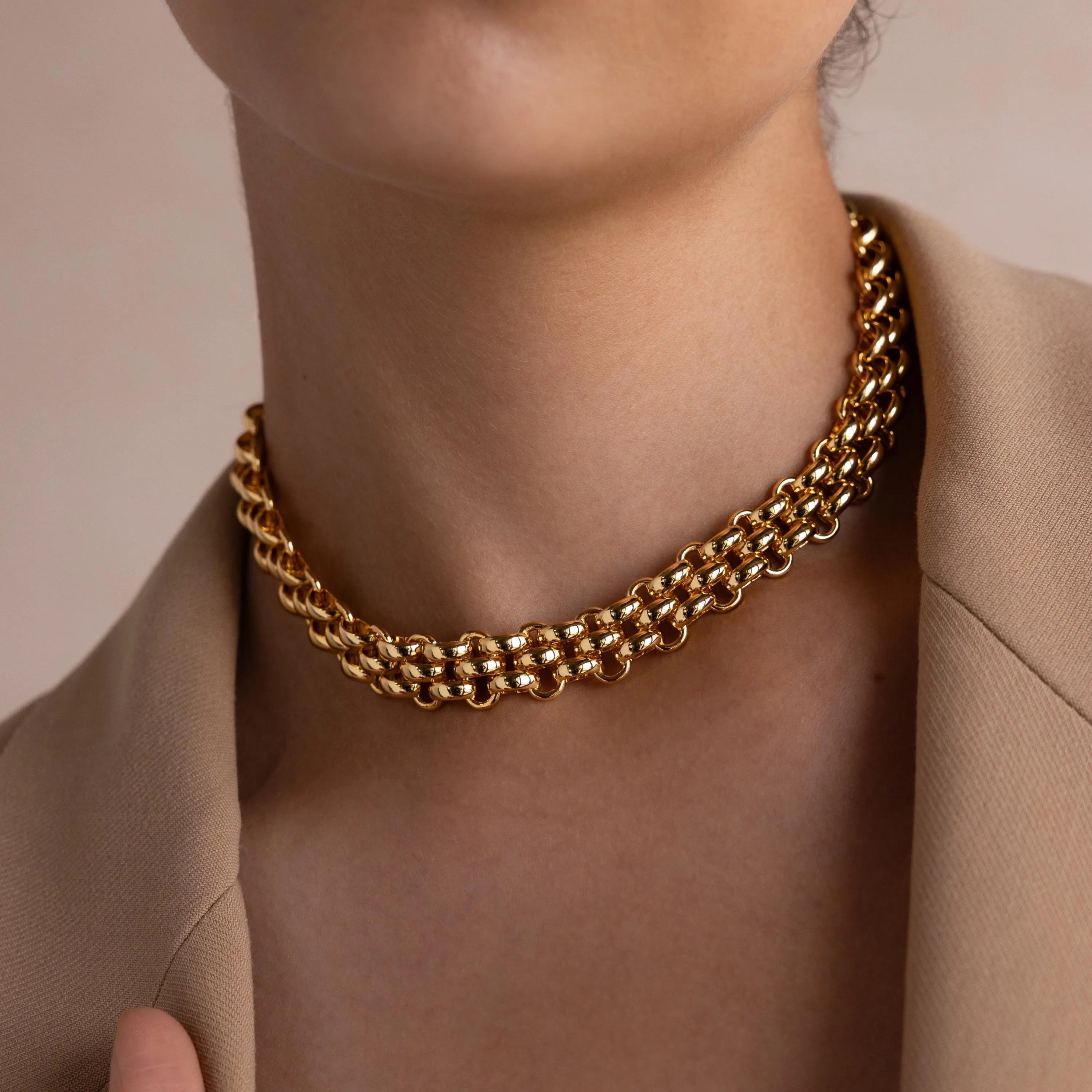 A person wears the Chunky Link Mesh Necklace, a bold gold chain choker, styled with a beige blazer and shown from the neck to upper chest.
