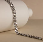 The Chunky Link Mesh Necklace is displayed draped over a white cylindrical object with a beige background, highlighting its bold and stylish jewelry design.