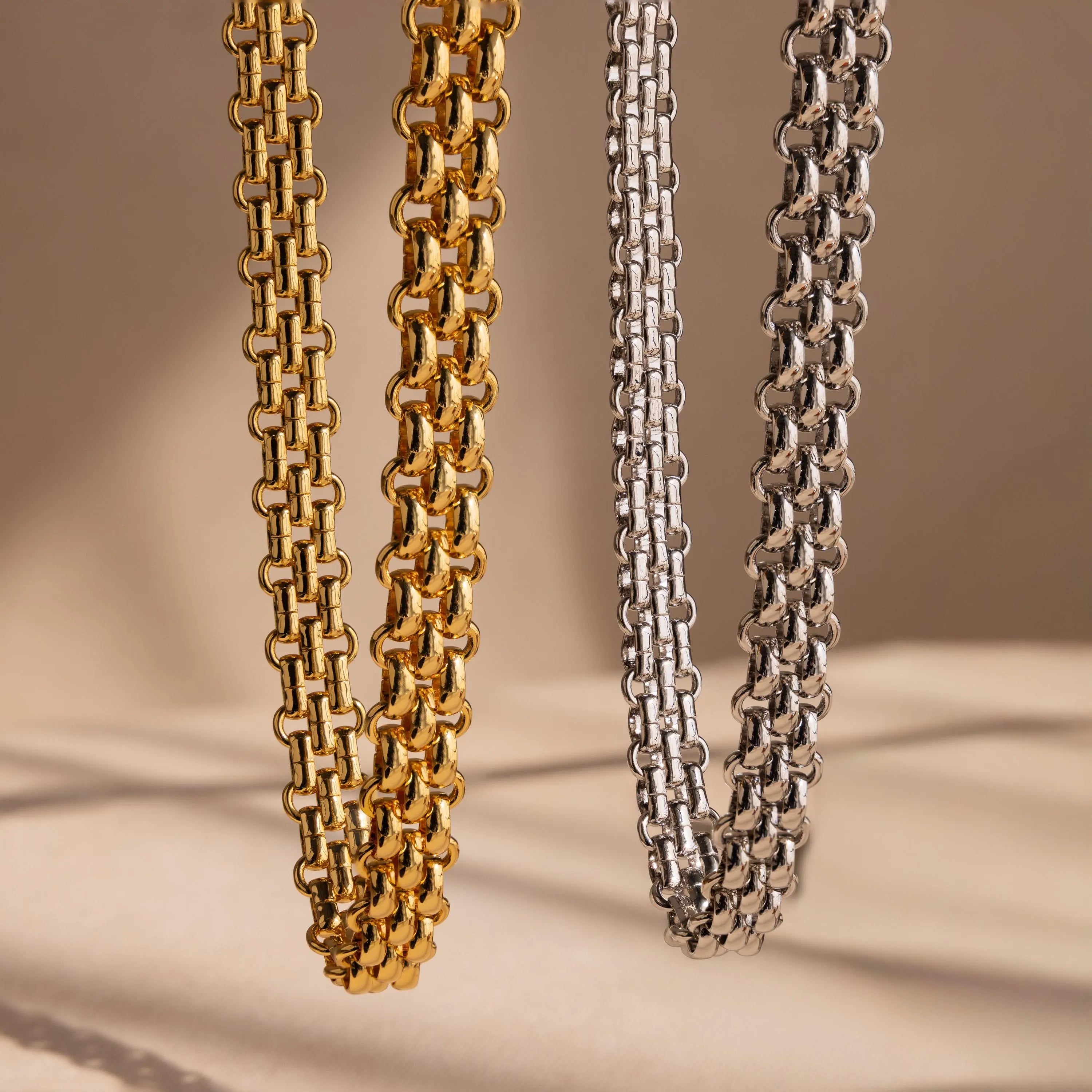 The Chunky Link Mesh Necklace, available in bold gold and silver tones, stands out as a statement piece against a neutral beige backdrop.