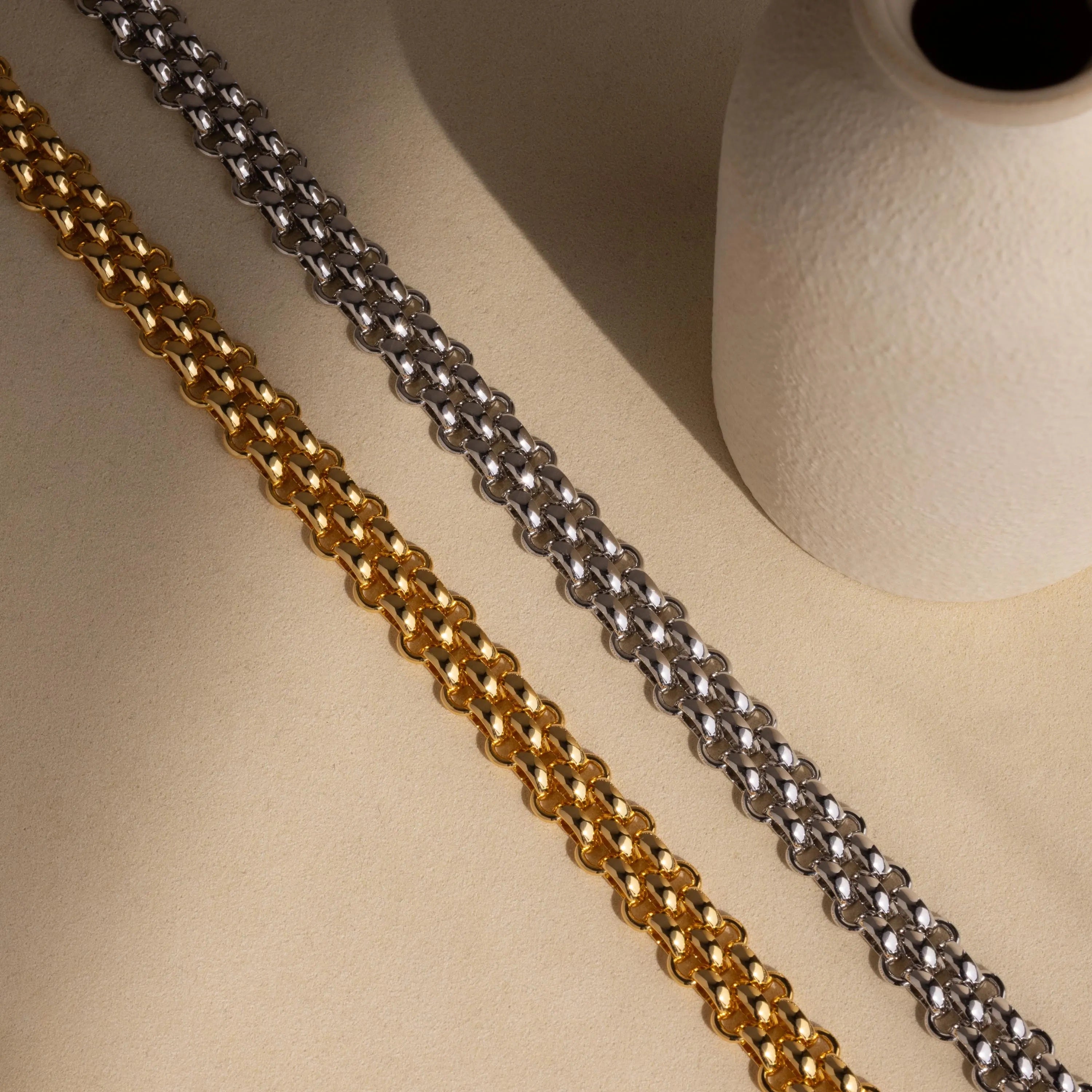 The Chunky Link Mesh Necklace is displayed diagonally next to a textured white ceramic vase on a beige surface—an eye-catching statement piece for bold jewelry styling.
