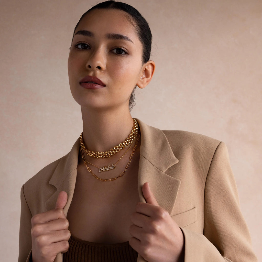 A woman in a beige blazer showcases the Chunky Link Mesh Necklace along with bold layered jewelry, posing against a soft, neutral background.