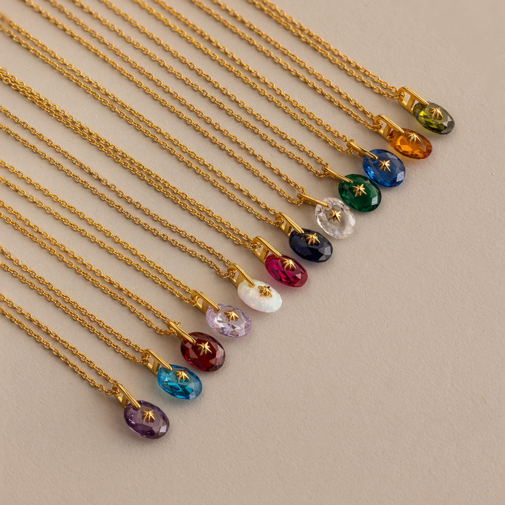 Close up of 12 Gold North Star Birthstone Pendant Necklaces laid out in a row.
