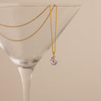 Gold North Star Birthstone Necklace with a Light Purple Alexandrite Gemstone hanging inside a cocktail glass.