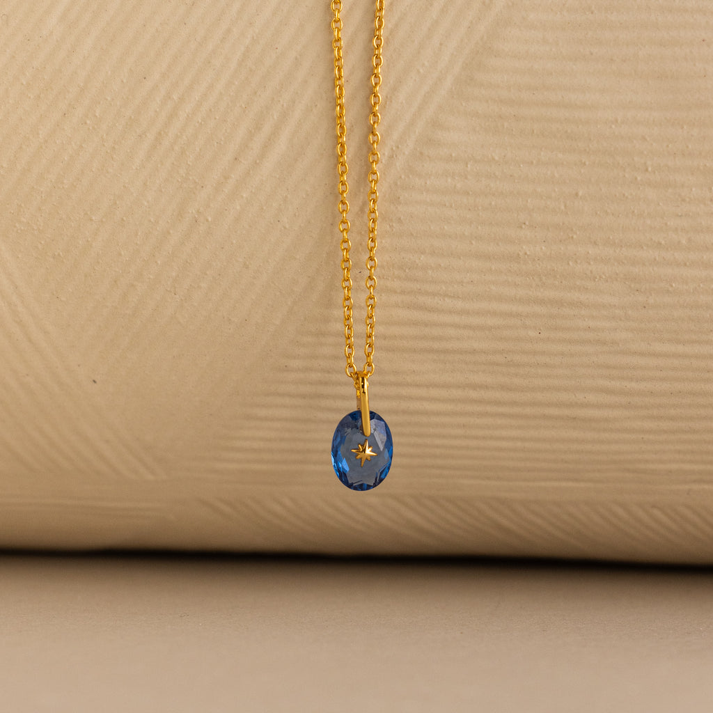 Close up of a Gold North Star Birthstone Necklace with a Blue Aquamarine Gemstone.