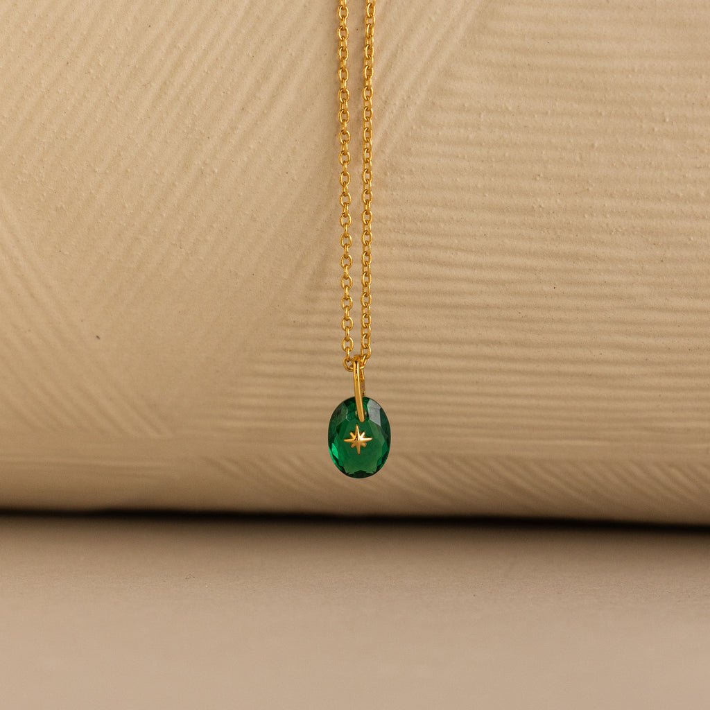 Close up of a Gold North Star Birthstone Necklace with a Green Emerald Gemstone.