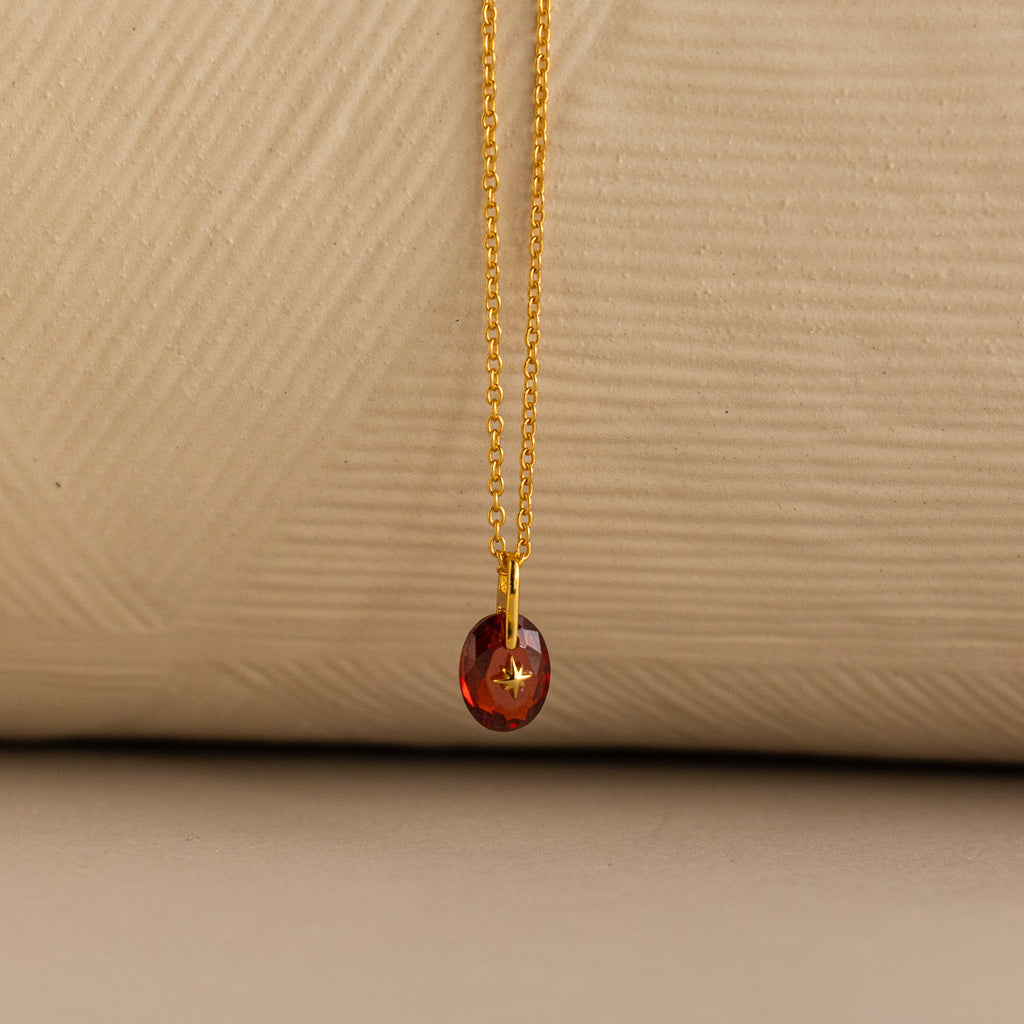 Close up of a Gold North Star Birthstone Necklace with a Red Garnet Gemstone.