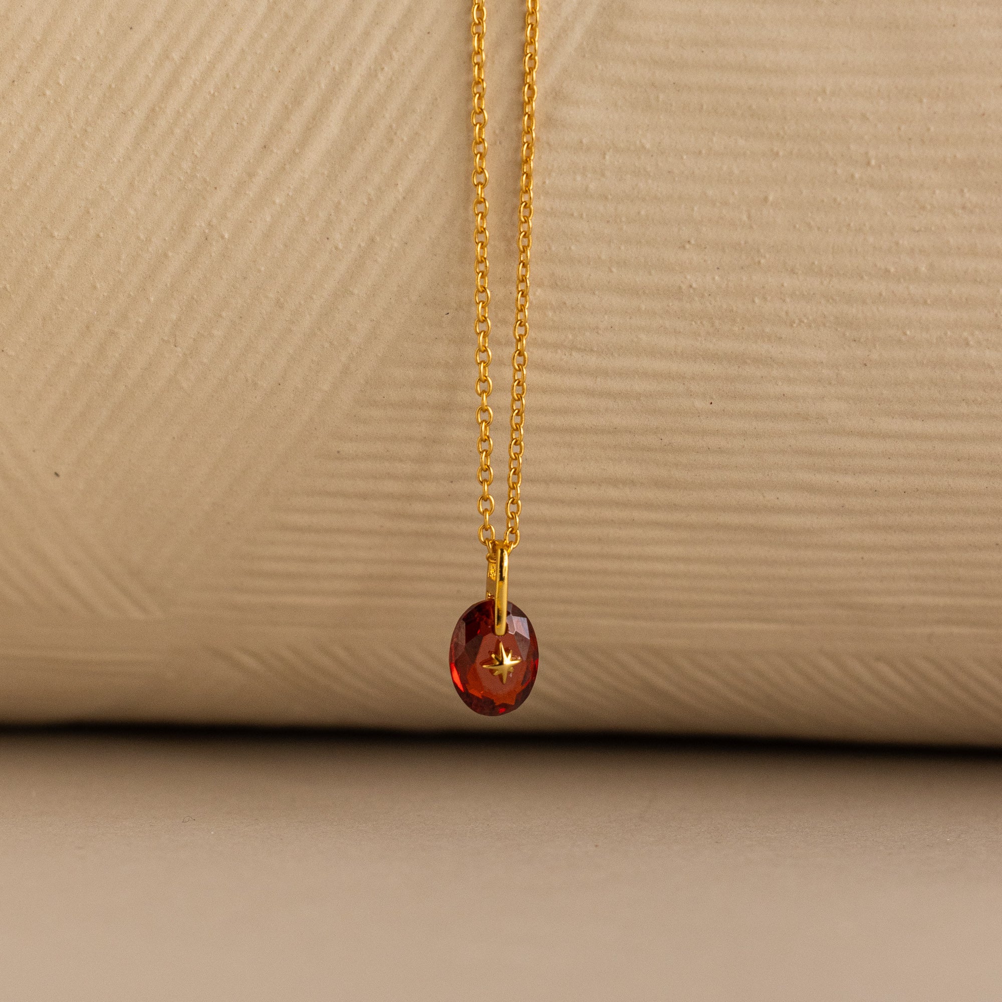 Close up of a Gold North Star Birthstone Necklace with a Red Garnet Gemstone.