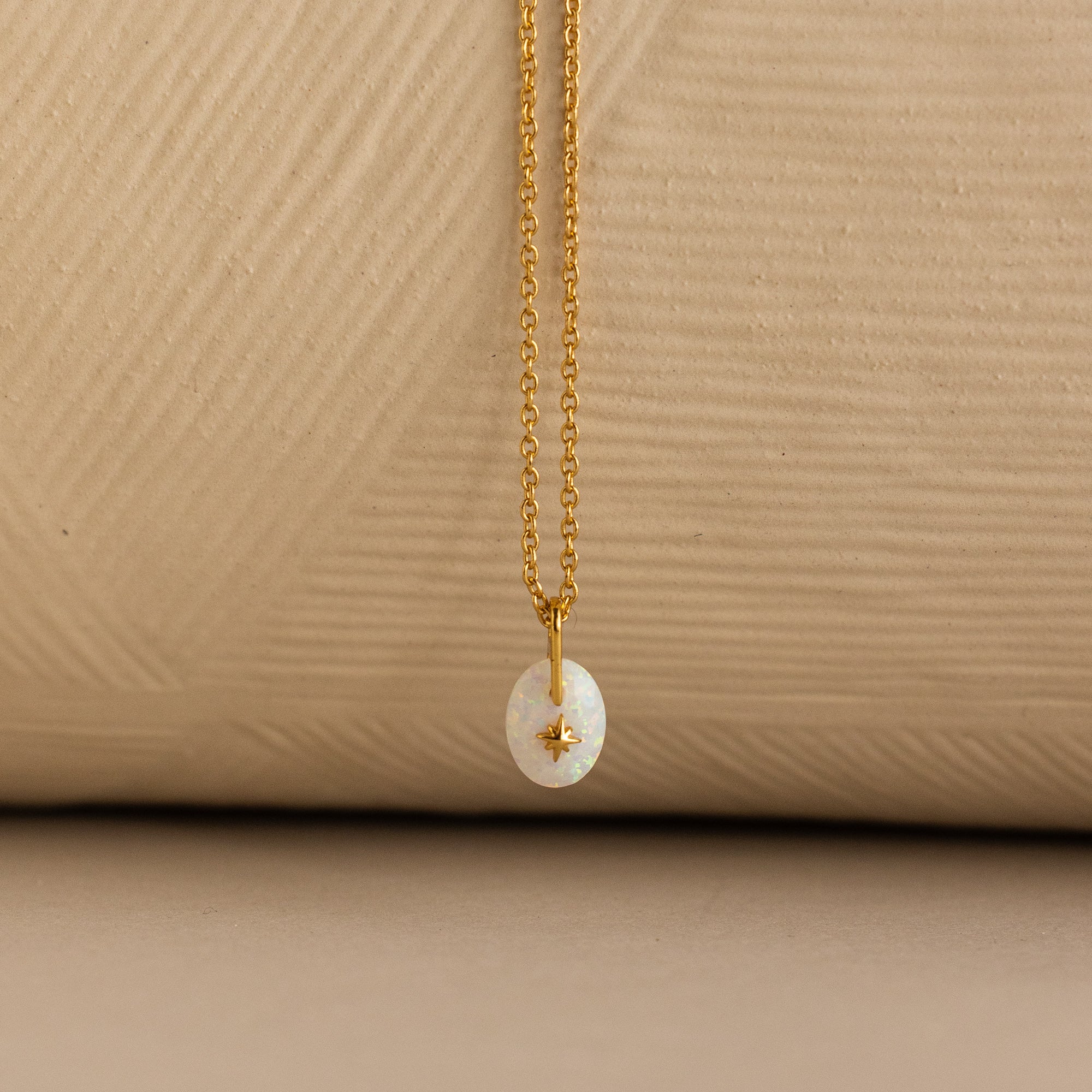 Close up of a Gold North Star Birthstone Necklace with a White Iridescent Opal Gemstone.