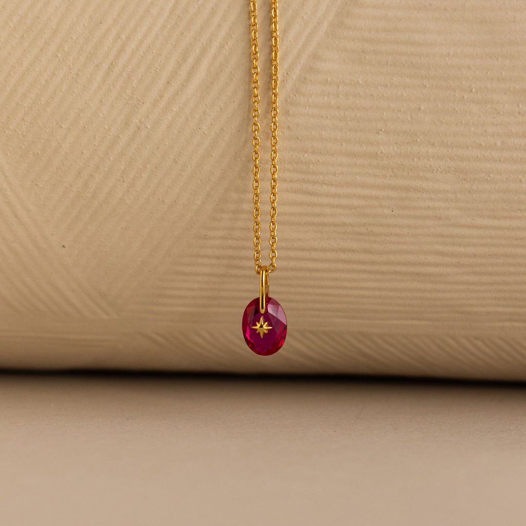 Close up of a Gold North Star Birthstone Necklace with a Pink Ruby Gemstone.