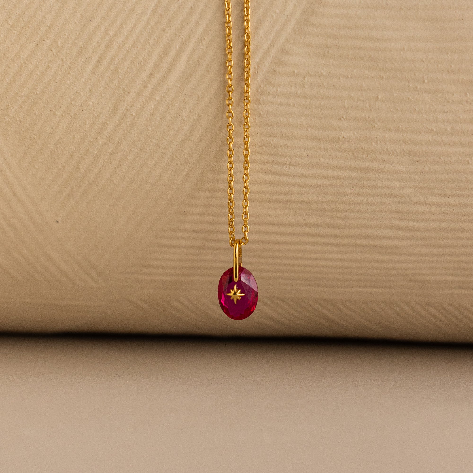 Close up of a Gold North Star Birthstone Necklace with a Pink Ruby Gemstone.
