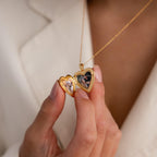 Model shows an open gold heart-shaped locket necklace containing two small photos.