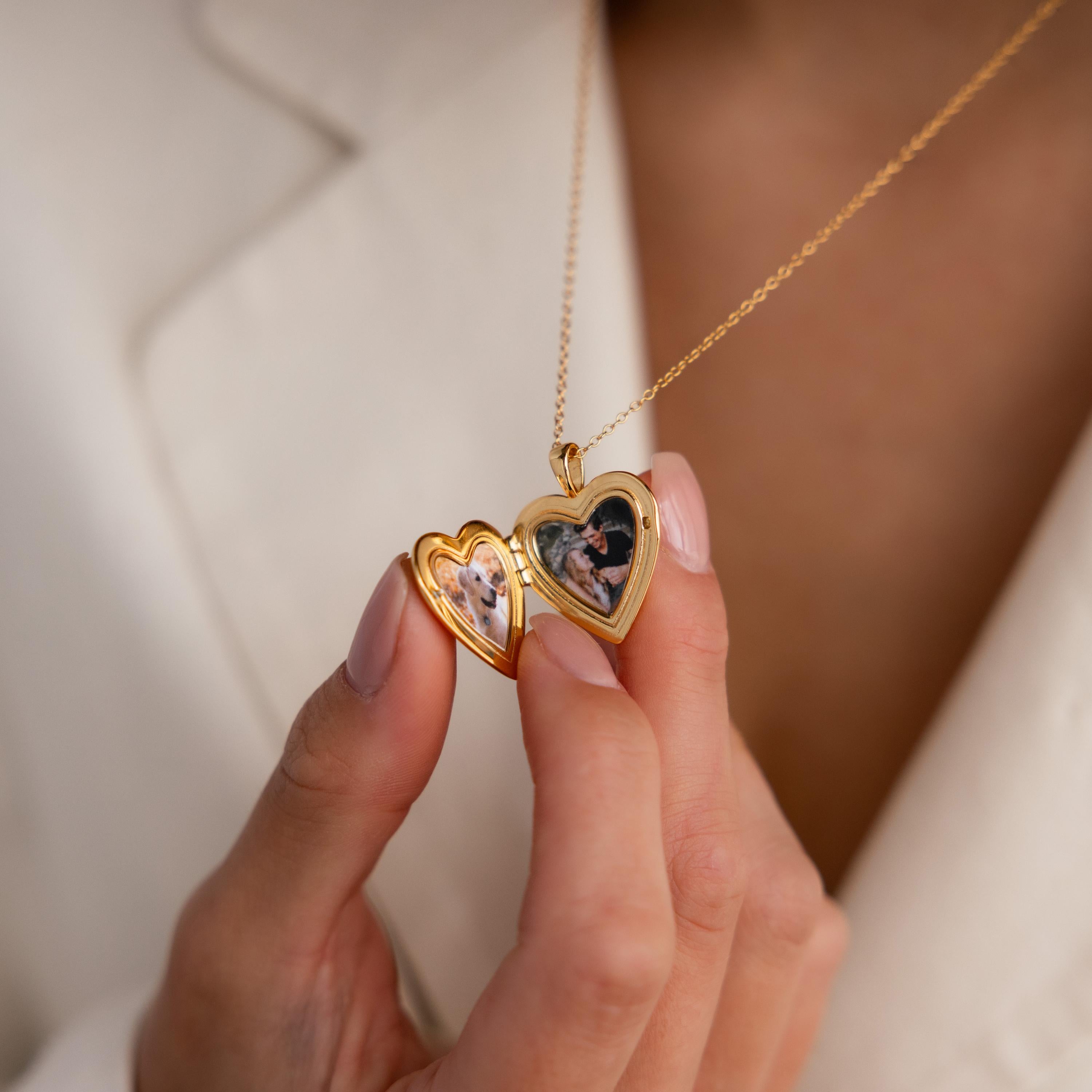 Model shows an open gold heart-shaped locket necklace containing two small photos.