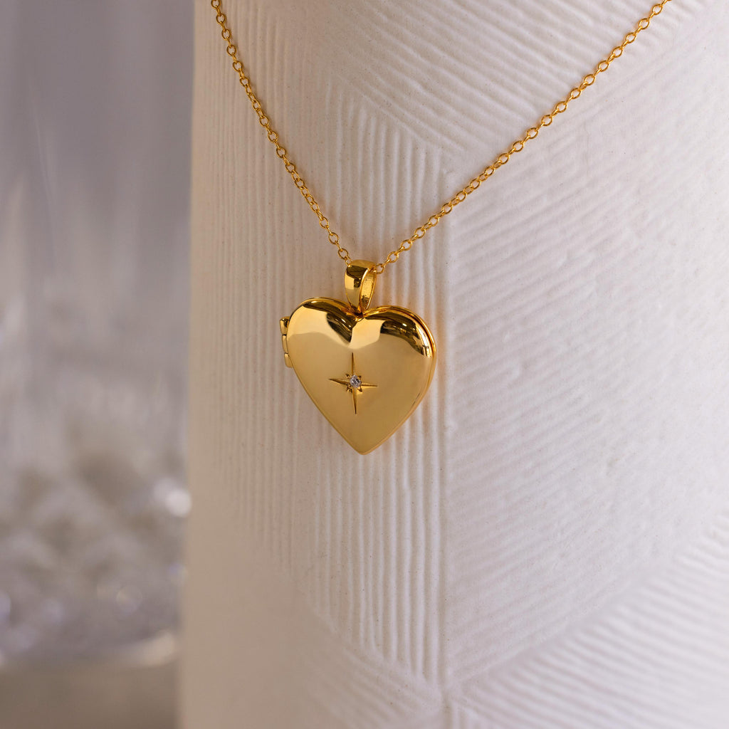 A gold heart-shaped locket with a north star CZ diamond in the center on a delicate cable chain.