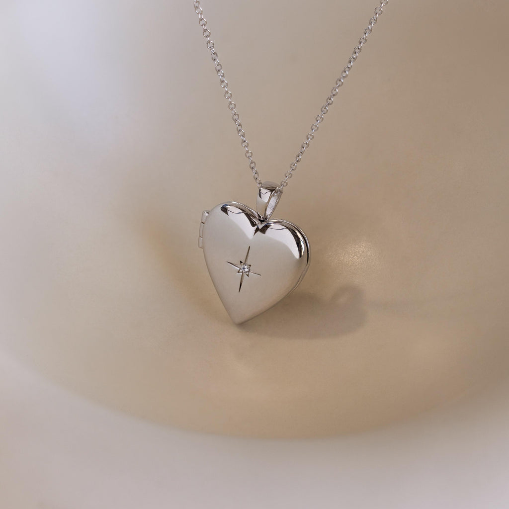 A silver heart-shaped locket with a north star CZ diamond in the center on a delicate cable chain.