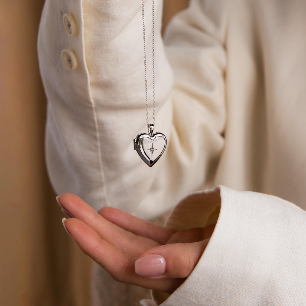 Model holding a silver heart-shaped locket necklace with a delicate north star CZ diamond.
