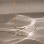 Two Pearl Curve Necklaces, ideal for bridal jewelry, are displayed on a beige surface—one features a gold chain and the other a silver chain.