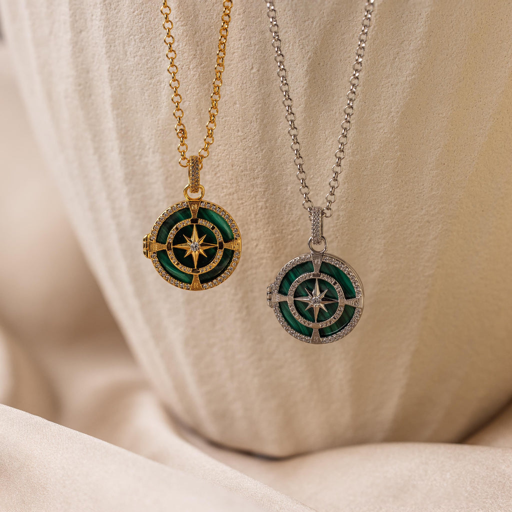 The Malachite Compass Locket Necklace, featuring green and white details, adds meaningful style as a guidance necklace or with a pavé diamond star—perfectly showcased on textured beige fabric.