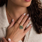 A woman wearing the Malachite Compass Locket Necklace with a striking green pendant rests her manicured hand on her chest.