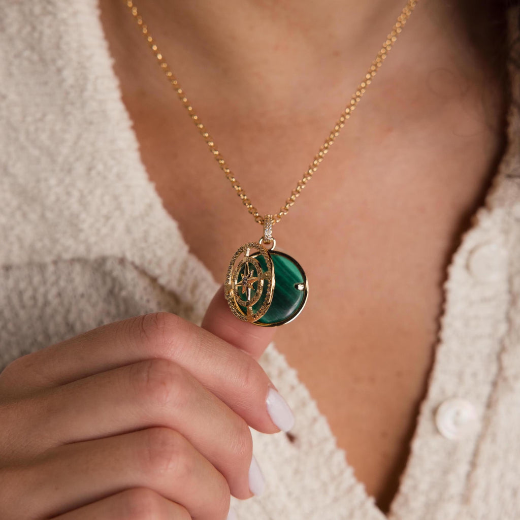 A person holds the Malachite Compass Locket Necklace, featuring a pavé diamond star, while wearing a textured cream top.