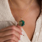 A person holds the Malachite Compass Locket Necklace, featuring a pavé diamond star, while wearing a textured cream top.