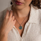 A woman touches her collar while wearing a cream textured button-up top and the Malachite Compass Locket Necklace.
