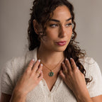 A woman with curly hair wears a cream knit top and gold jewelry, including a pavé diamond star ring and her signature Malachite Compass Locket Necklace.
