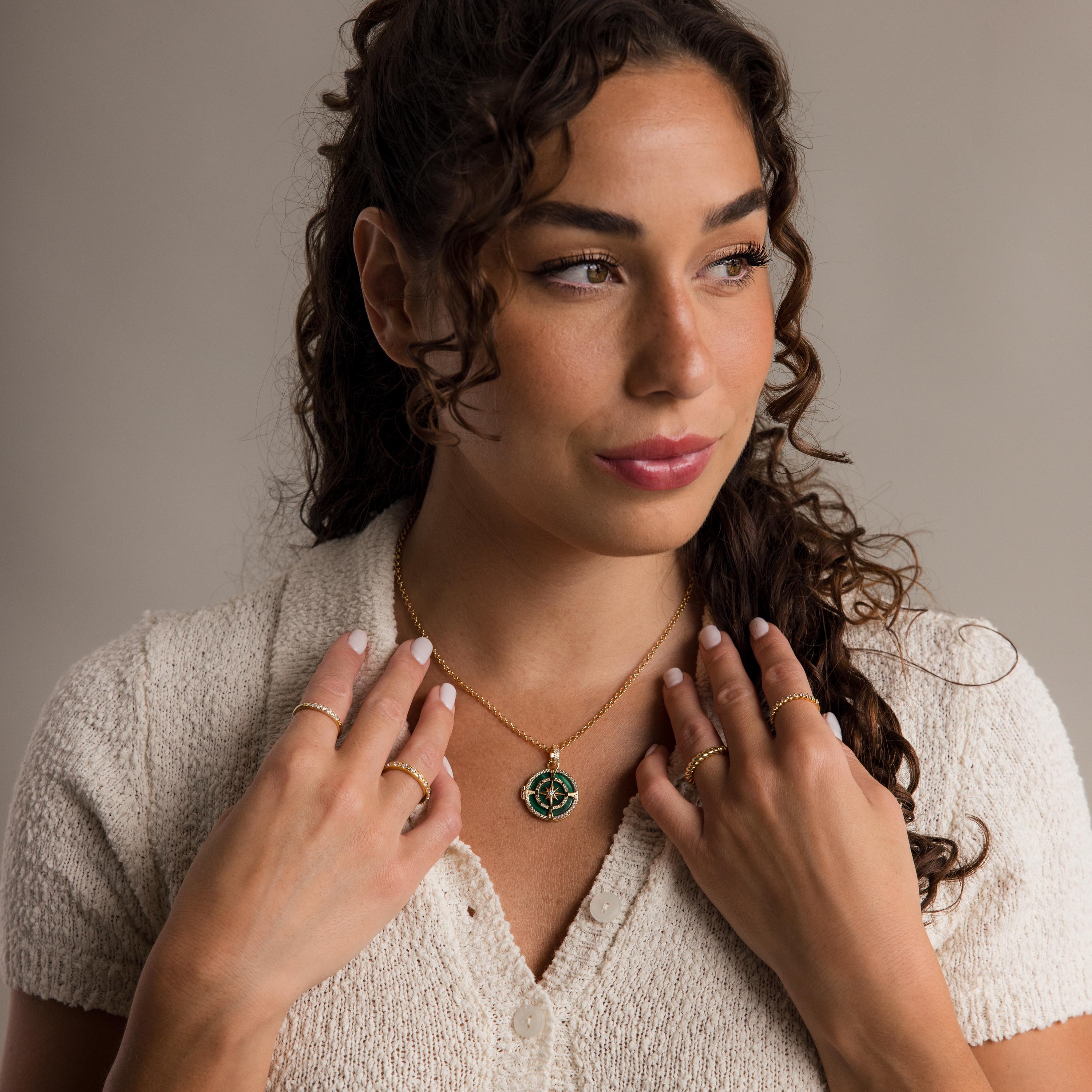 A woman with curly hair wears a cream knit top and gold jewelry, including a pavé diamond star ring and her signature Malachite Compass Locket Necklace.