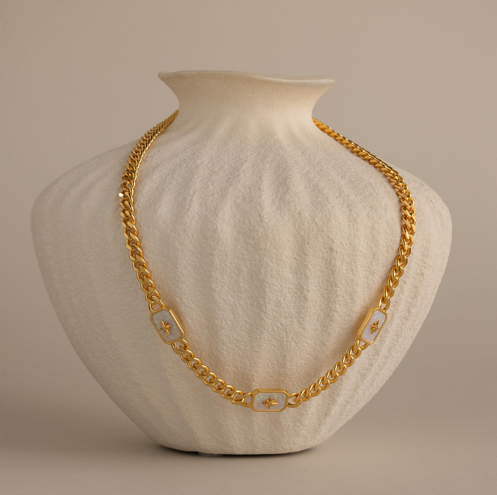 Gold North Star Opal Necklace displayed on a textured cream vase.