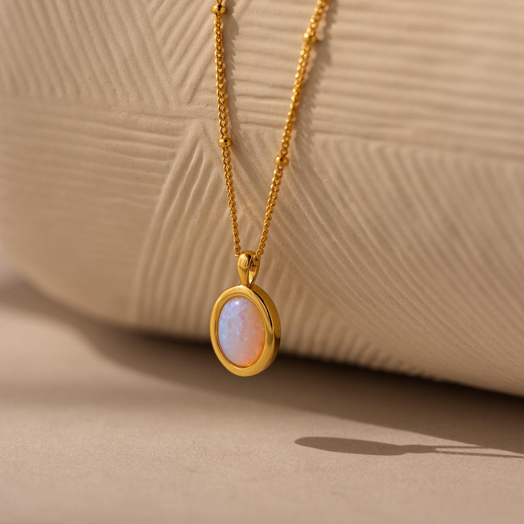 Opal Pendant Necklace: Showcasing an oval Opal gemstone on a fine gold satellite chain, beautifully presented against a textured beige background.