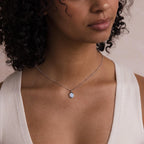 A woman wearing a white top and the Opal Pendant Necklace, featuring a round opal gemstone on a delicate satellite chain.
