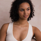A woman with curly hair, wearing a white top and the Opal Pendant Necklace on a delicate satellite chain, gazes softly to the side.