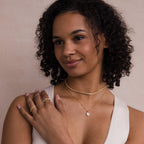 Smiling woman with curly hair wears a cream sleeveless top and layered gold necklaces, featuring the Opal Pendant Necklace.