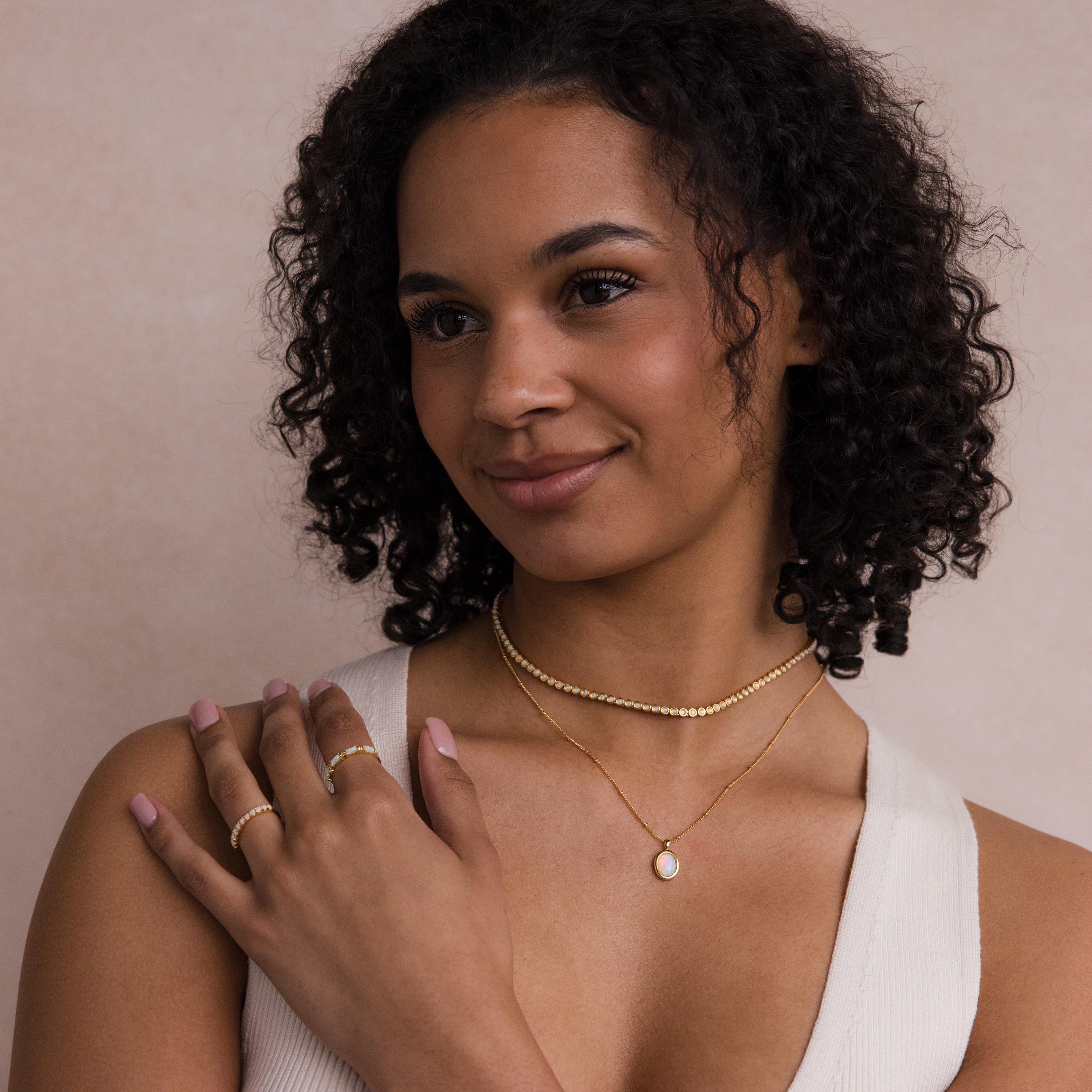 Smiling woman with curly hair wears a cream sleeveless top and layered gold necklaces, featuring the Opal Pendant Necklace.