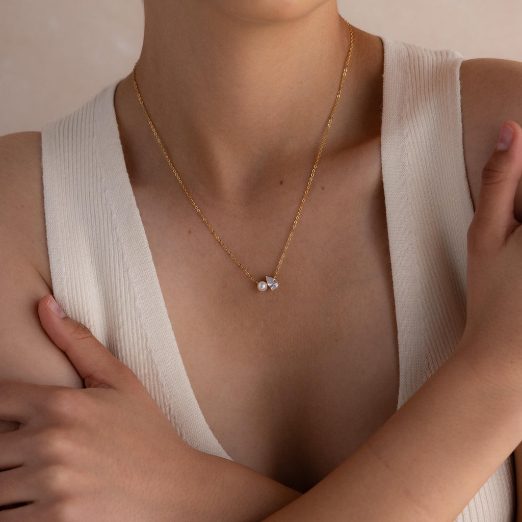 Woman wearing the Pearl Diamond Necklace, featuring a gold chain with a delicate teardrop diamond pendant, paired with a sleeveless white top with a deep neckline.