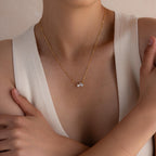 Woman wearing the Pearl Diamond Necklace, featuring a gold chain with a delicate teardrop diamond pendant, paired with a sleeveless white top with a deep neckline.