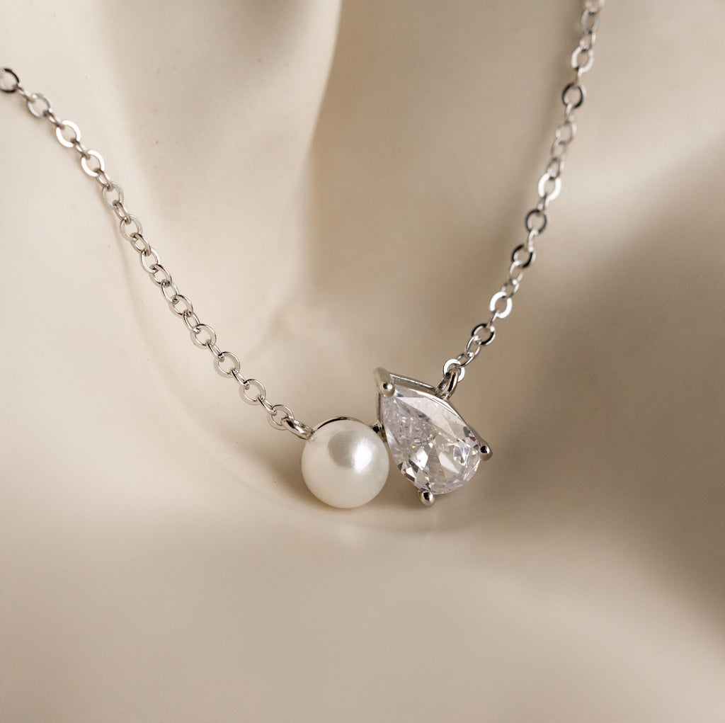 The Pearl Diamond Necklace showcases a luminous pearl and sparkling teardrop diamond pendant in Toi et Moi style, elegantly displayed on a light, smooth surface.