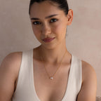 A woman with dark hair in a bun wears a cream sleeveless top and the Pearl Diamond Necklace, featuring a delicate design with a small pendant.